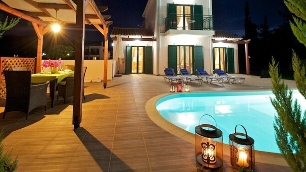 Una casa de dos pisos con piscina, mobiliario exterior y un patio cubierto.