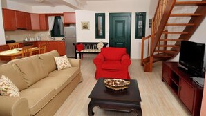 Una sala de estar con un sofá, un sillón rojo, una mesa de centro, un televisor y una escalera.