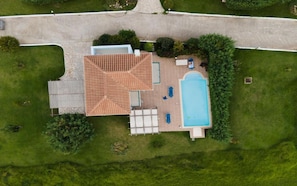 An aerial view of a house with a swimming pool, a patio with seating, and a lawn.