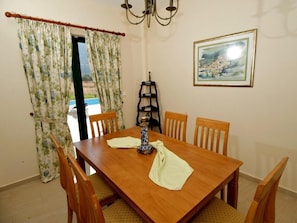 A dining room with a wooden table, chairs, a chandelier, a painting, and a window with curtains.