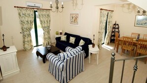 Un salon comprenant un canapé, un pouf à rayures, une table à manger avec des chaises et un lustre.