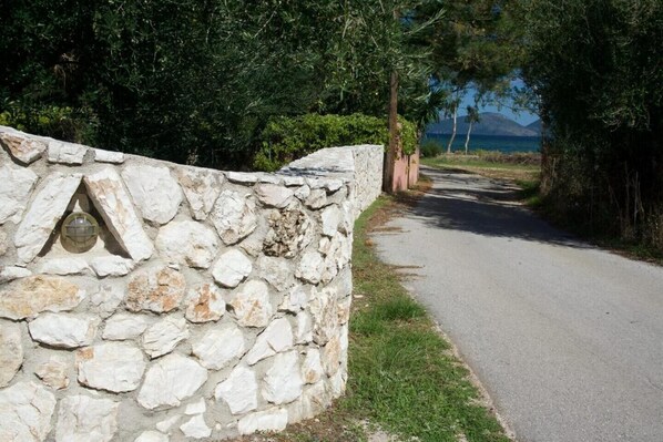 Un mur de pierre avec une fenêtre, une route pavée et une vue sur la mer et les montagnes.