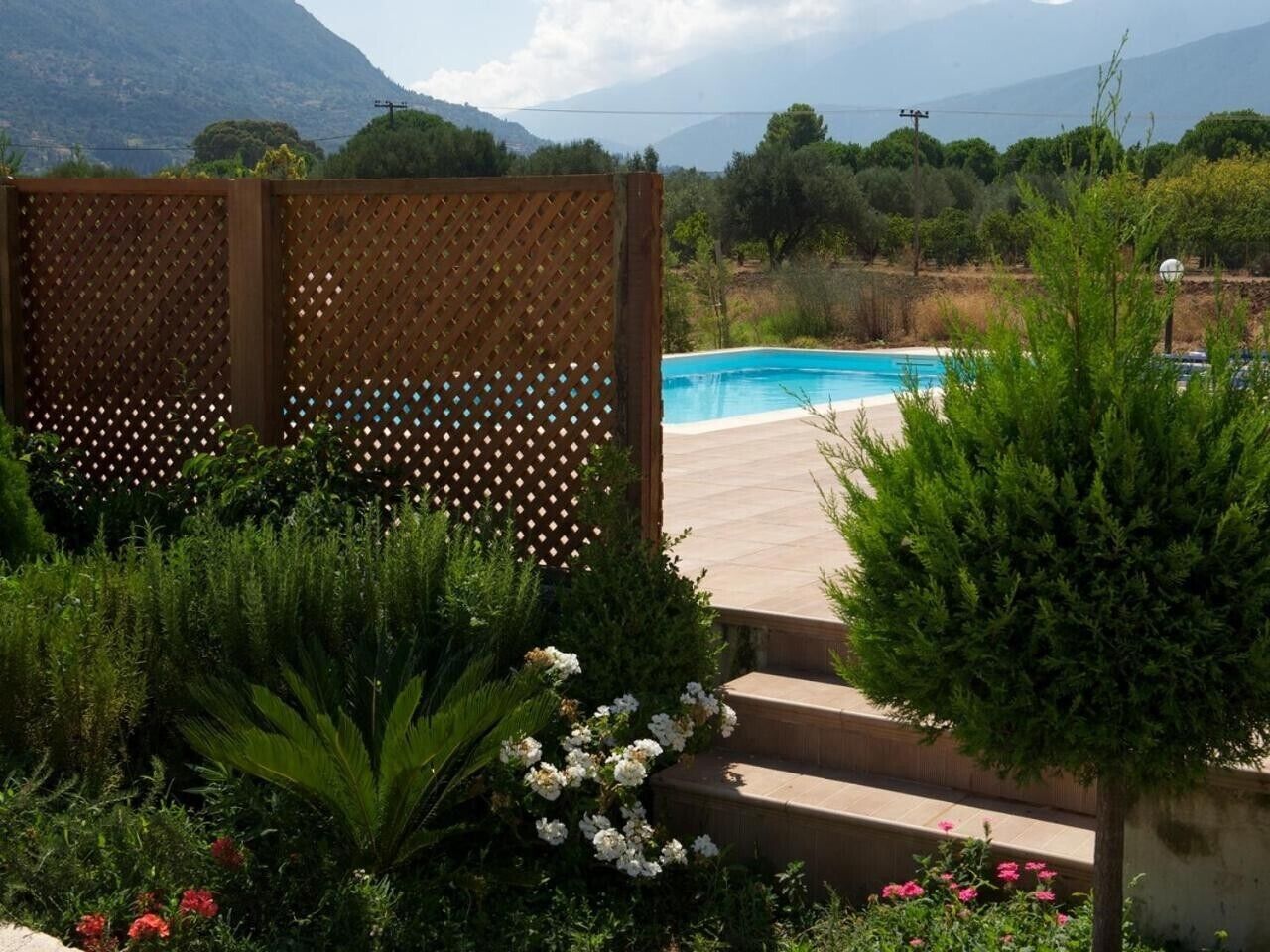 A pool area with a wooden deck, surrounded by lush greenery and a mountainous backdrop.