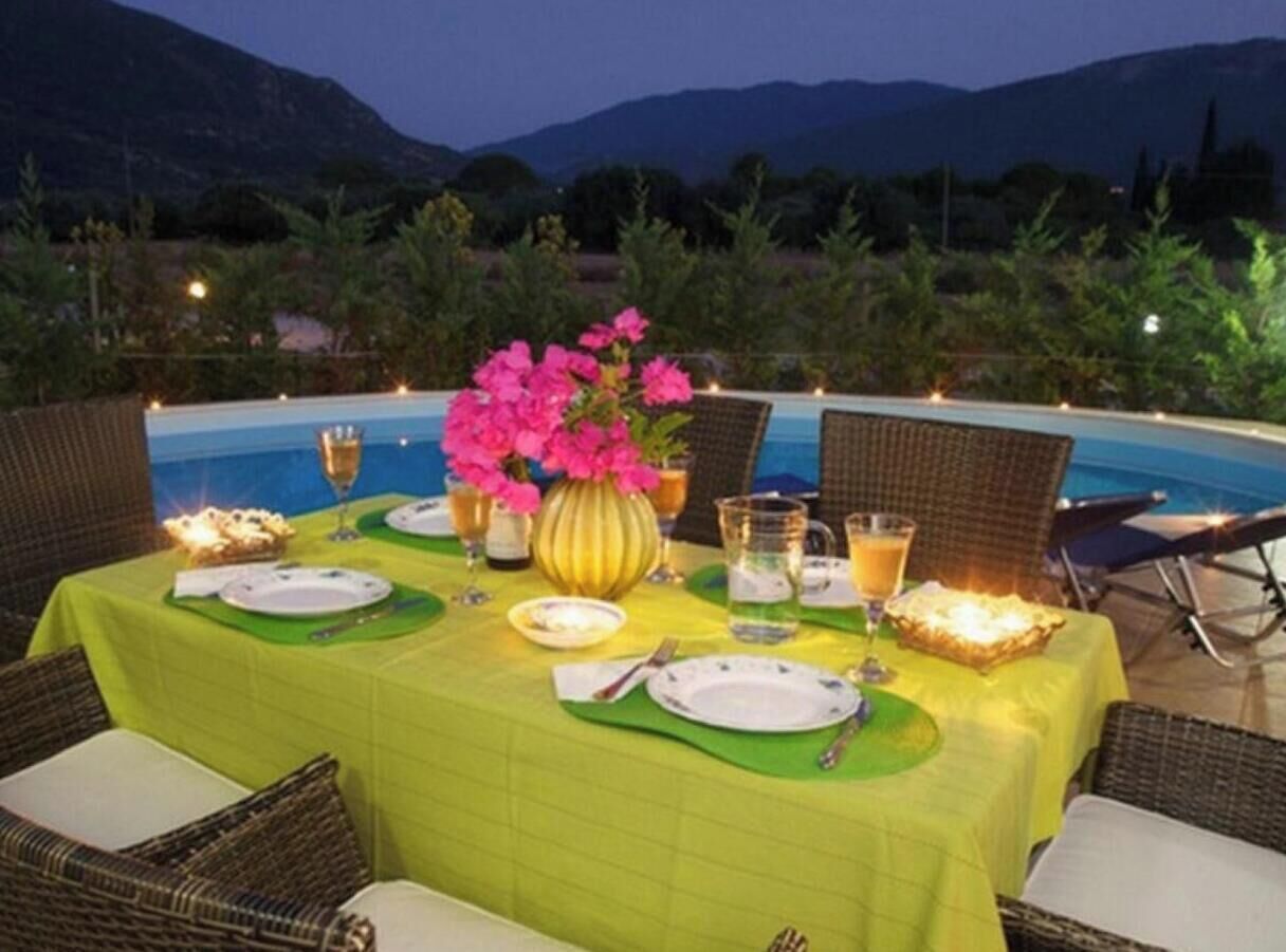 A dining table set for two with a green tablecloth, plates, cutlery, and a vase of pink flowers.