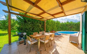 Une terrasse extérieure avec une table et des chaises en bois, un barbecue et une piscine.