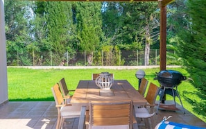 An outdoor patio with a wooden table and chairs, a decorative lantern, and a barbecue grill.