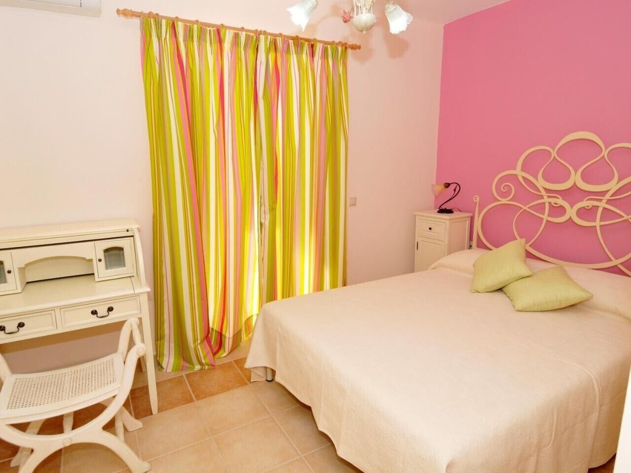 A bedroom with a bed, a desk, a chair, a nightstand, and a curtain.