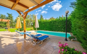 A covered outdoor area with a pool, lounge chairs, and umbrellas.