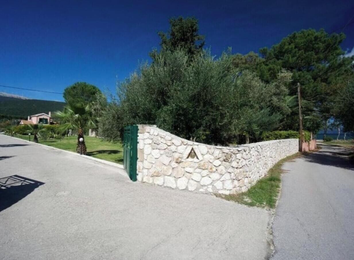 A stone wall with a green gate, a clear sky, and trees in the background.