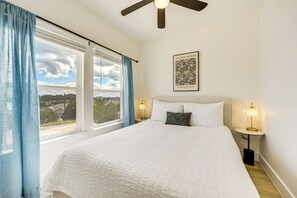Relax in comfort with a large bed, ceiling fan, and framed artwork, plus a window with a view of the outdoors.