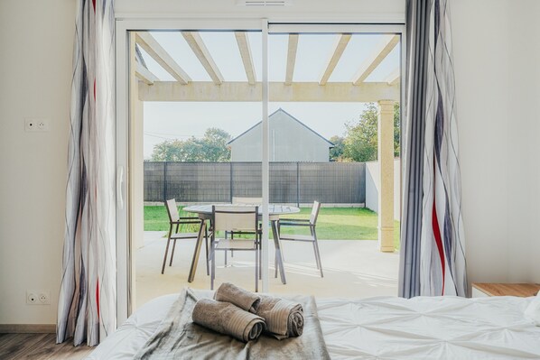A bedroom with a large window, a bed, and a view of an outdoor patio area.