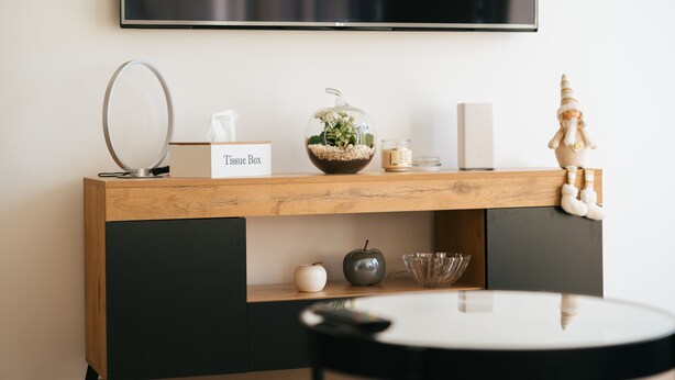 Una habitación moderna con una mesa consola de madera, una caja de pañuelos, un cuenco decorativo de vidrio, una manzana pequeña, un cuenco de vidrio y una figurita de madera.