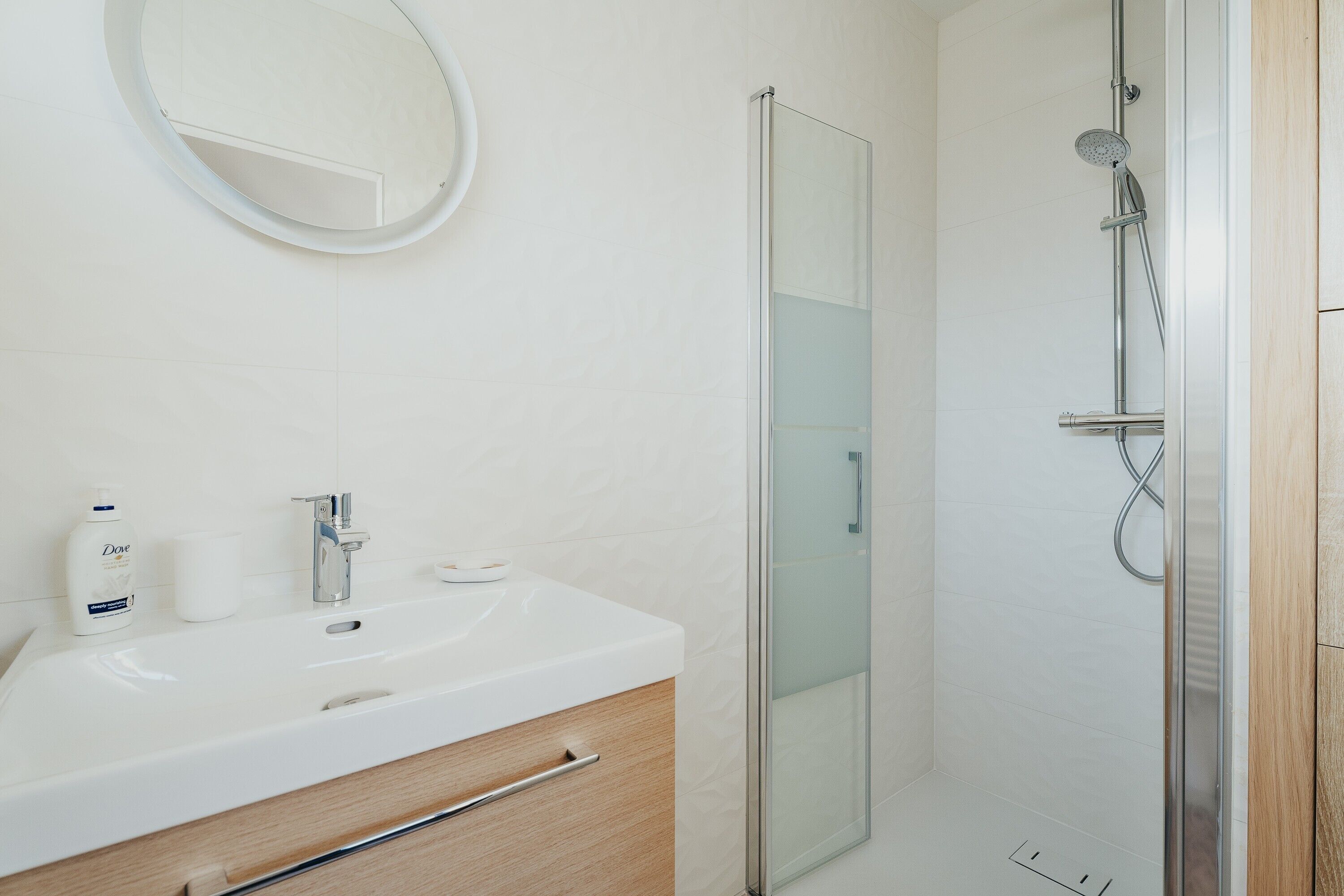 Een badkamer met een witte wastafel, spiegel en een douchecabine van glas.