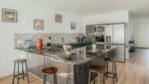 Una cocina moderna con una isla central, taburetes de bar, un refrigerador y un microondas.