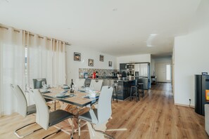 Un espace de repas moderne avec une longue table, des chaises et une cuisine en arrière-plan.