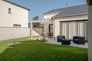 Une maison moderne dotée d’une pelouse bien entretenue, d’un espace extérieur aménagé pour se détendre et d’un garage.