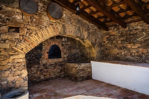 Una habitación con paredes de piedra, chimenea de ladrillo, techo de madera y un banco blanco.