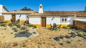 Un bâtiment blanc avec un toit en tuiles, un chemin de pierre et du mobilier d’extérieur.