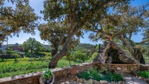 Une structure en pierre surmontée d’une croix, entourée de verdure et d’arbres.