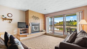 Una sala de estar con chimenea, televisor y un ventanal grande con vistas a un lago.