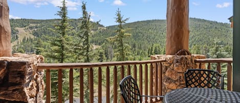 A wooden deck with a table and chairs, overlooking a forested valley.