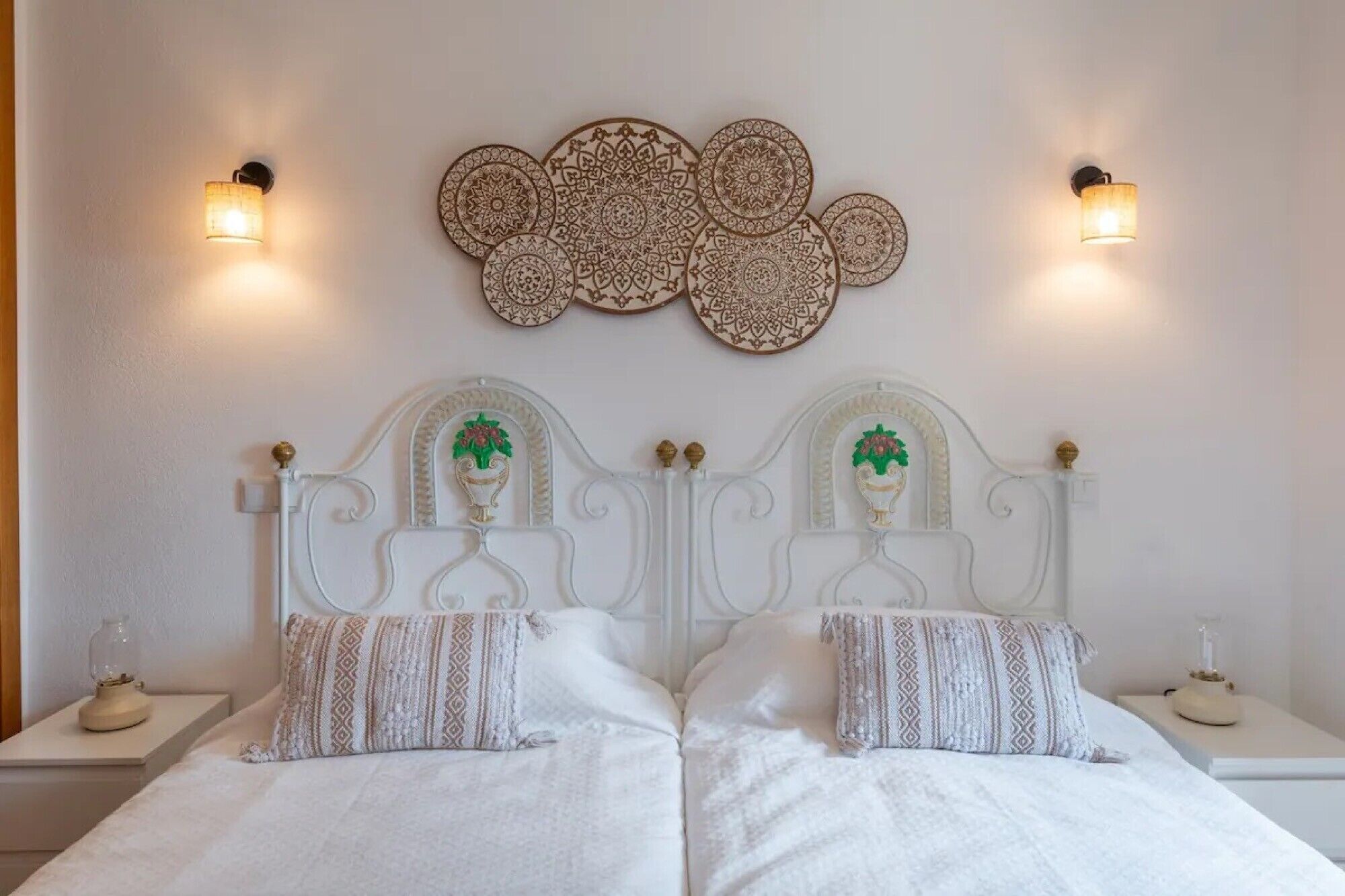 A double bed with a white headboard, two wall sconces, and a decorative wall piece above.
