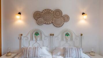 A double bed with a white headboard, two wall sconces, and a decorative wall piece above.