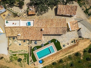 Oversigtsbillede af en ejendom med swimmingpool, flere rum med flisebelagte tage og en anlagt have.