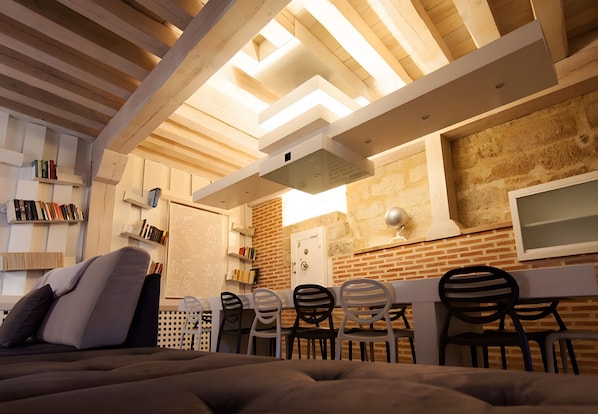 A room with a bed, a desk, and chairs, with bookshelves and a television.