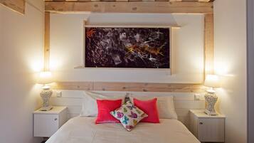 Un dormitorio con cama, dos mesitas de noche, una obra de arte colgada en la pared y techo de madera.
