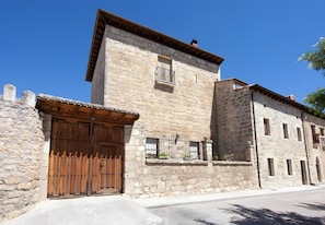A stone building with a wooden door, a window with a metal railing, and a small balcony with potted plants.