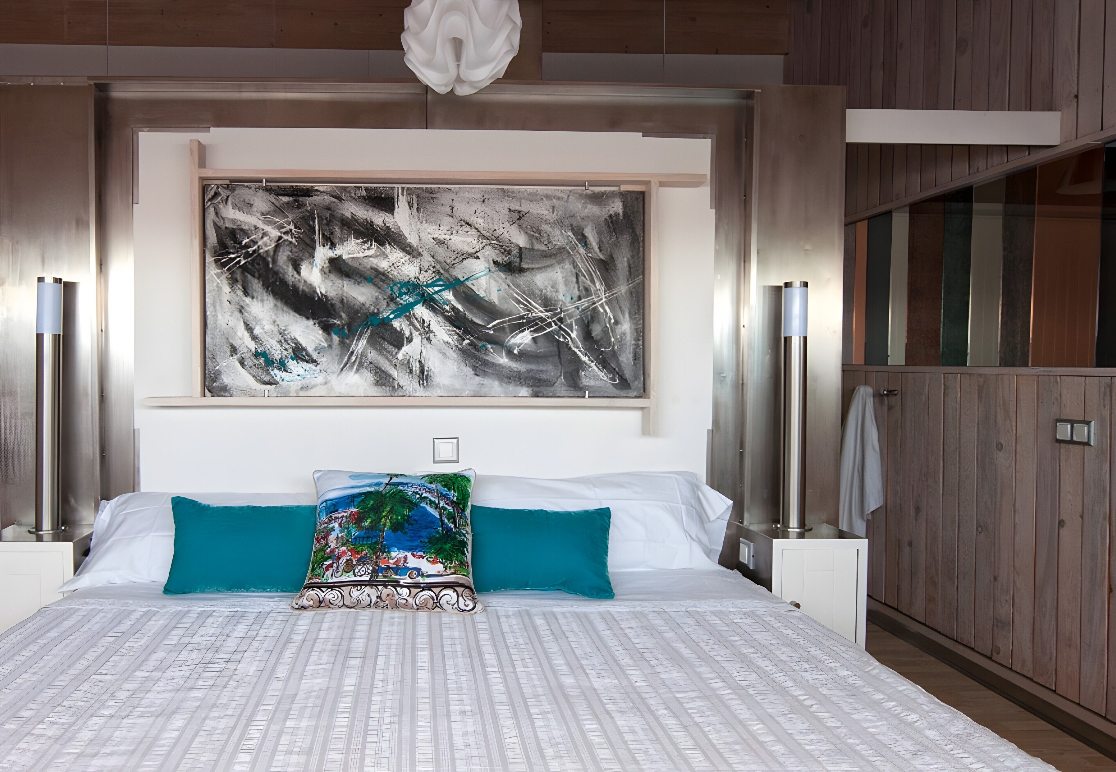 A modern bedroom with a large abstract painting, a patterned bedspread, and a view of a wooden interior.