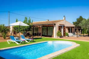 Una casa con piscina, un patio con sillones de descanso y un área de estar al aire libre techada.