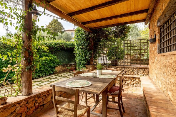 Une terrasse extérieure avec une table et des chaises en bois, entourée de murs en pierre et de verdure.