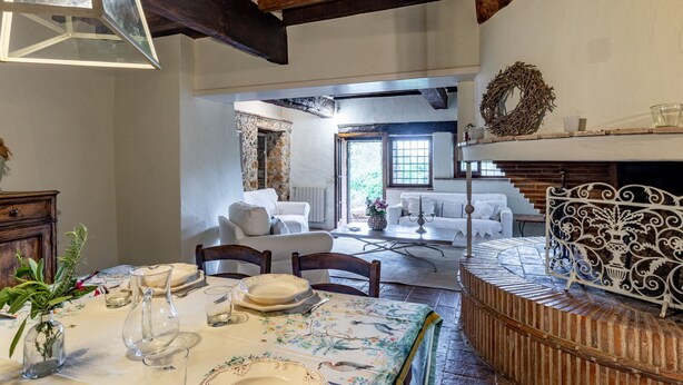 A dining area with a table set for four, a fireplace, and a view into a living room with a sofa and a window. - Holiday Home 'Greg's House' with Private Pool, Garden and Wi-Fi (Santa Lucia)