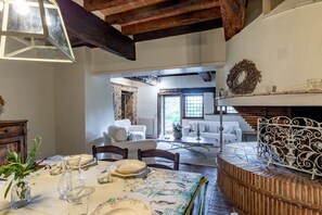 Un coin repas avec une table dressée pour quatre personnes, une cheminée et une vue sur un salon comprenant un canapé et une fenêtre.