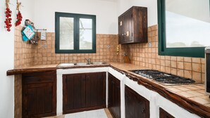 A kitchen with a window, wooden cabinets, a stove, and a tiled backsplash. - Villa 'Sa Curcurica' with Sea View, Private Terrace and Wi-Fi (Orosei)