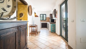 A kitchen with a tiled floor, wooden cabinets, a small wooden cart, and a window with a view. - Villa 'Sa Curcurica' with Sea View, Private Terrace and Wi-Fi (Orosei)