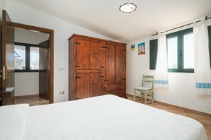 A bedroom with a bed, wooden wardrobe, chair, and a window with curtains.