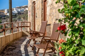 A stone building with a balcony, wooden chairs, and a view of the surrounding landscape.