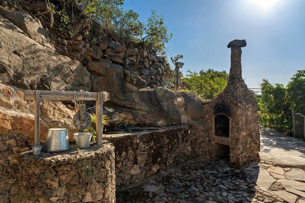 A rustic outdoor setting with a stone wall, a metal grill, and a chimney structure.