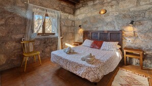 Ein Schlafzimmer mit Stehwänden, einem Bett, einem Stuhl, einem Fenster mit Vorhängen und zwei Nachttischlampen.