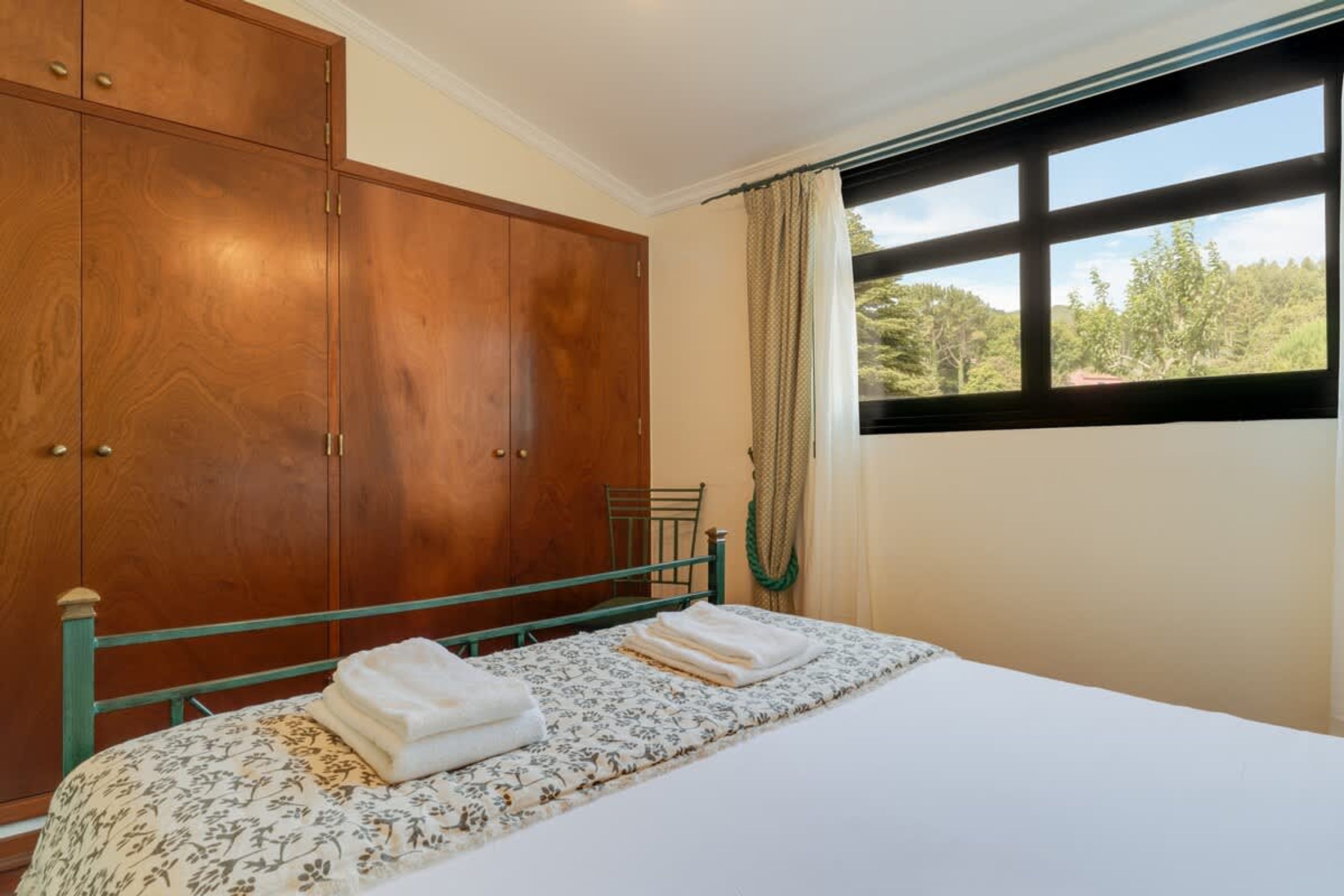 Une chambre à coucher avec un lit, une armoire en bois et une fenêtre donnant sur des arbres.