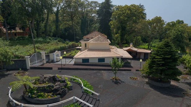 A building with a tiled roof, surrounded by a landscaped area with trees and shrubs. - Quinta dos Abutitos in Santo Ant nio da Serra (Santa Cruz)