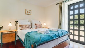 A bedroom with a bed, bedside tables, a nightstand, a window with curtains, and a picture on the wall. - Quinta dos Abutitos in Santo Ant nio da Serra (Santa Cruz)