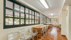 A long corridor with a series of windows, a wooden table, and metal chairs. - Quinta dos Abutitos in Santo Ant nio da Serra (Santa Cruz)