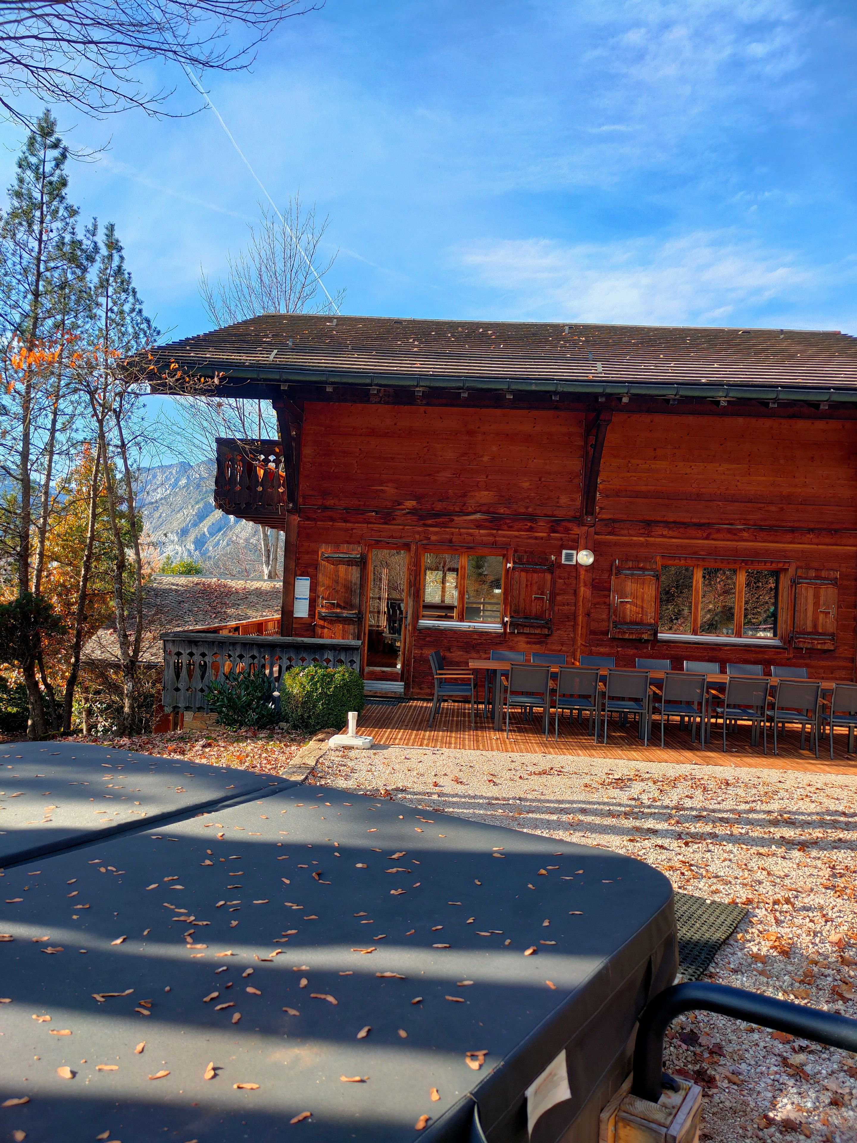Een rustiek houten gebouw met een overdekt terras, een eettafel met stoelen en een uitzicht op bergen.
