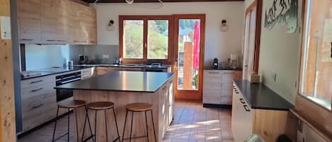 A modern kitchen with a large island, bar stools, wooden cabinets, and a view through the door.
