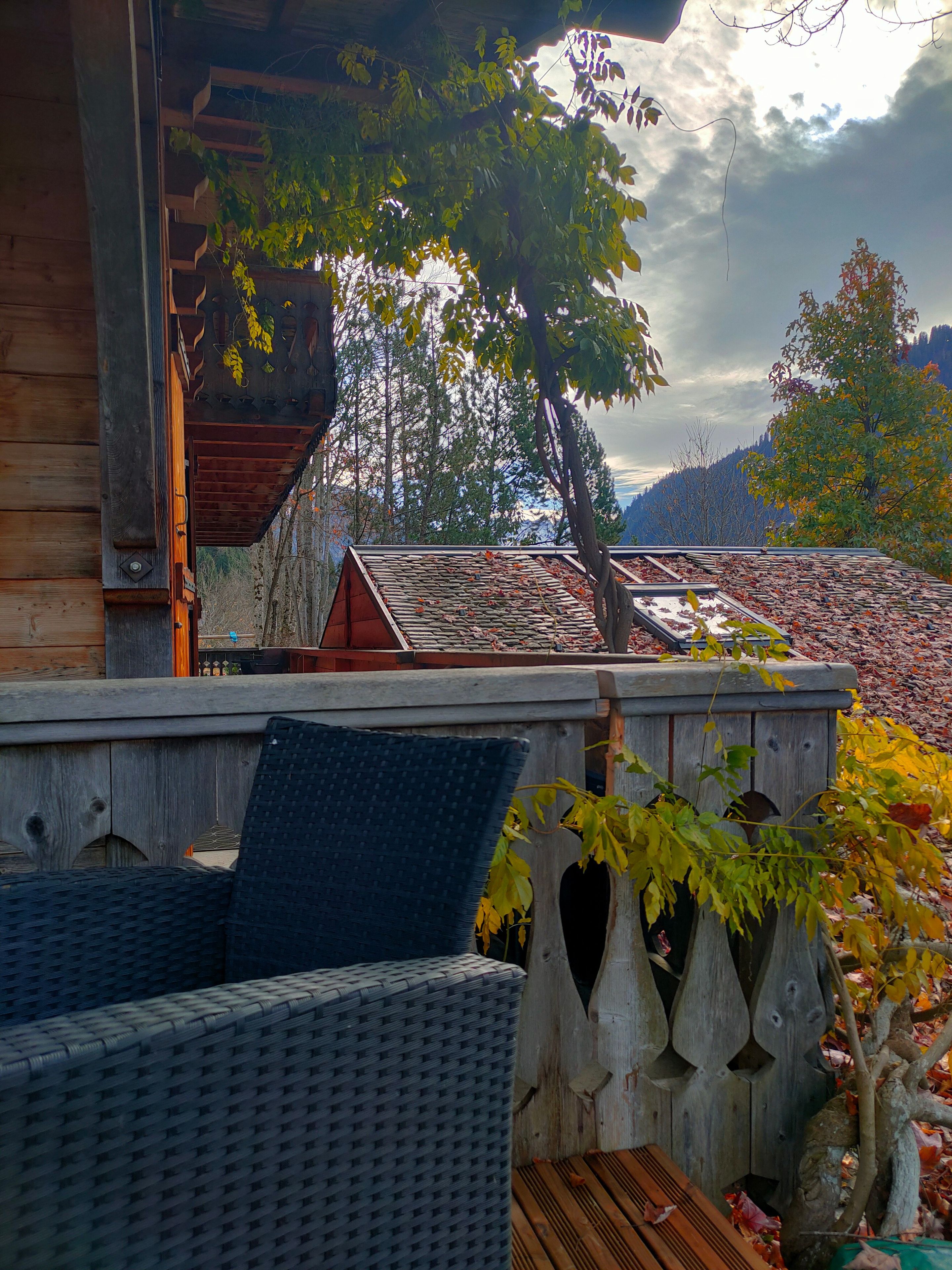 A wooden deck with a wicker sofa and a table, surrounded by a wooden fence and trees.