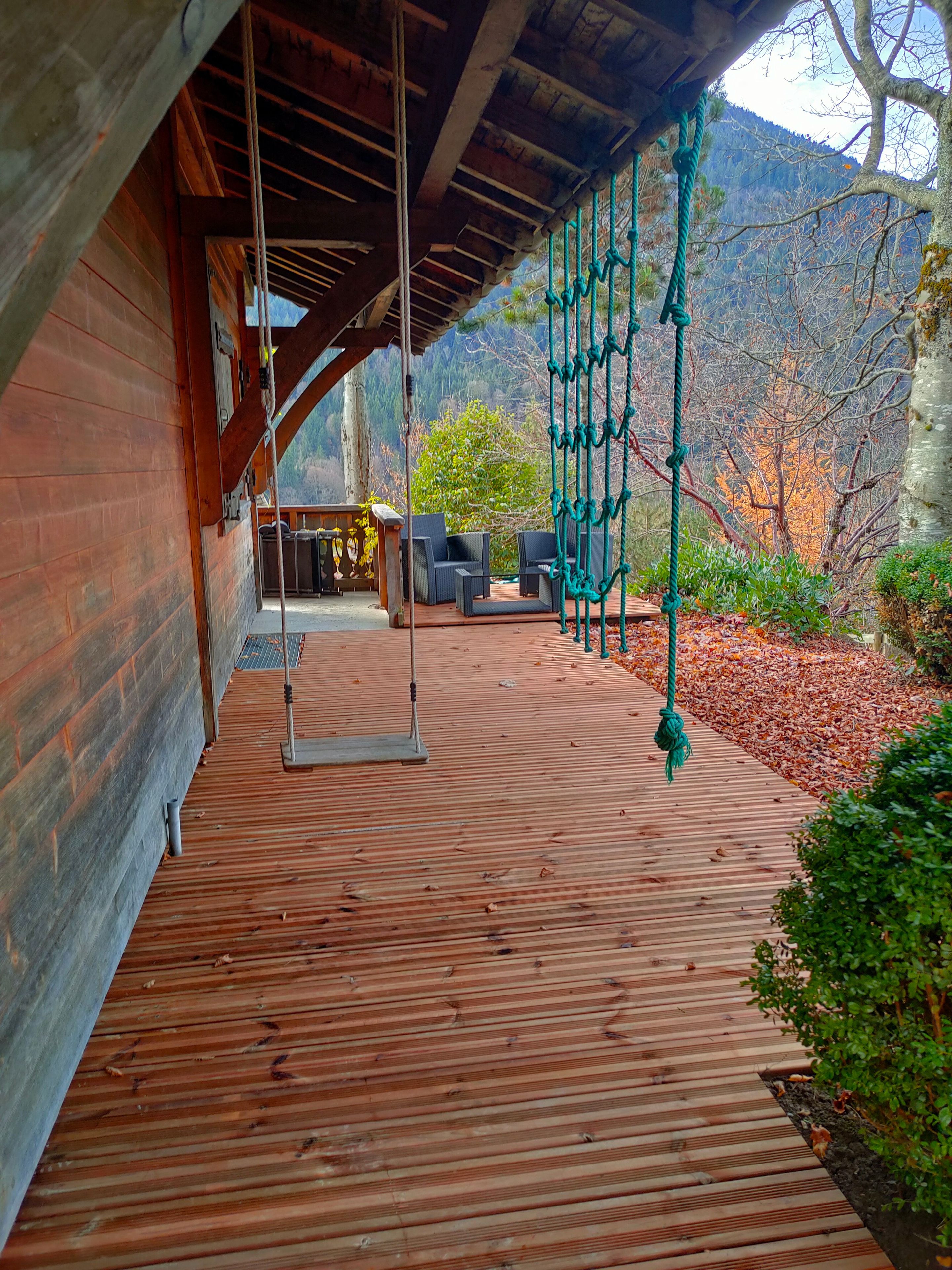 Eine Holzterrasse mit Schaukel und Gartenmöbeln, mit Blick auf eine gebirgige Landschaft.